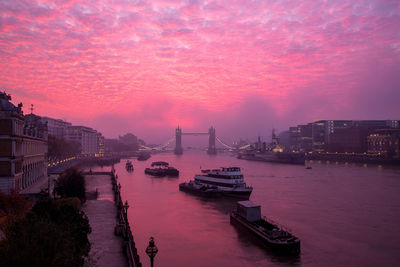 Boats in river against buildings at sunset