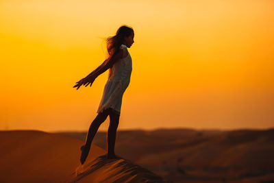 Side view of silhouette woman standing on land against sky during sunset