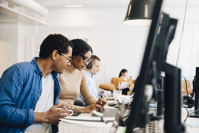 It professionals discussing over laptop on desk while sitting creative office