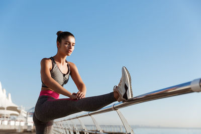 Young woman sitting against clear blue sky