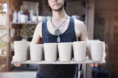 Midsection of craftsman holding clay containers at workshop