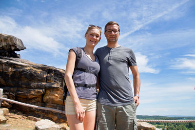 Low angle portrait of smiling young couple standing against sky