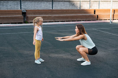 Woman teaching squats to daughter at sports court