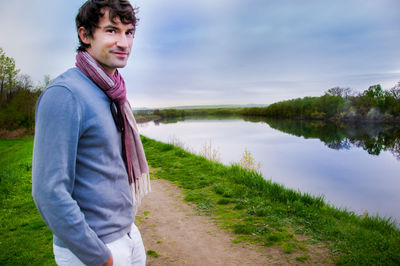 Side view of young man standing by lake against sky