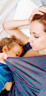 High angle view of young woman breastfeeding child on bed at home