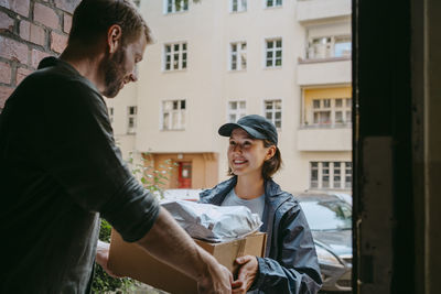 Smiling female delivery person giving packages to man while standing at doorway