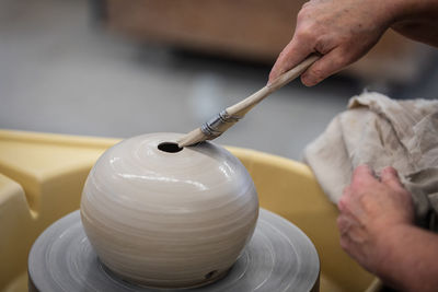 Artist's cropped hands glazing raku pottery with a brush on a spinning throw wheel