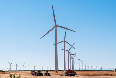 Windmills on field against clear blue sky
