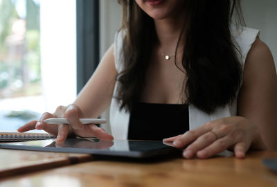 Midsection of woman using digital tablet on table