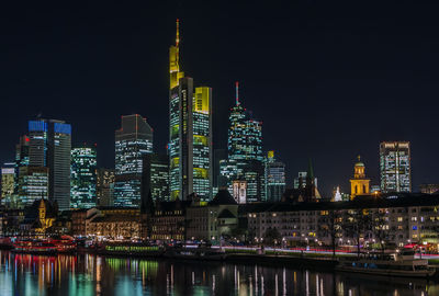 Illuminated buildings by river against sky in city at night