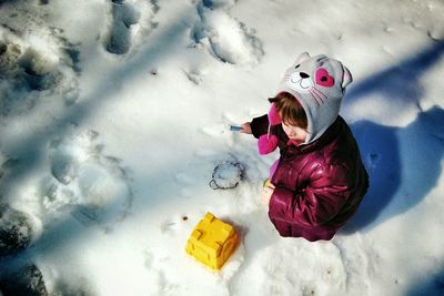 High angle view of girl crouching on snow covered field in park