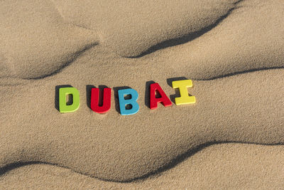 Dubai word written with colorful letters on soft sand of the desert