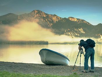 Man is taking photo of ship at mountain lake shore. silhouette at fishing paddle boat at lake coast