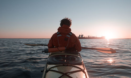 Sea kayak trip. back view. active lifestyle. a sailing ship in the background
