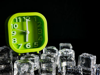 Close-up of clock over ice cubes against black background