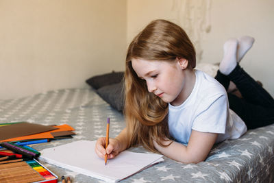 The girl after school plays at home, draws with pencils and felt-tip pens