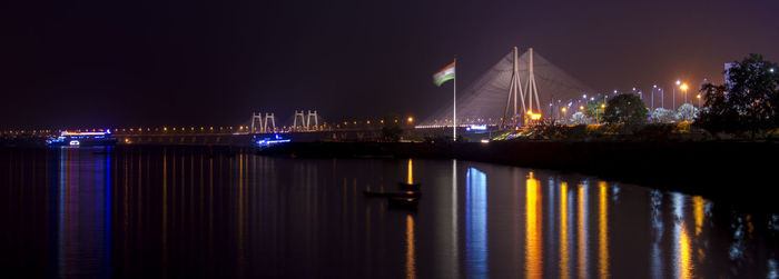 Illuminated bridge over river with buildings in background at night