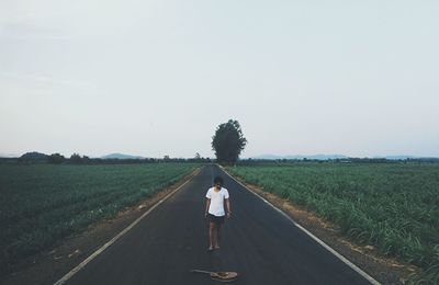 Man standing on road amidst field against sky