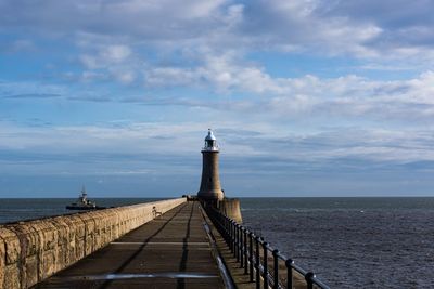 Lighthouse on pier by sea against sky