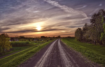 Road amidst field against sky during sunset