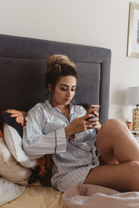 Young woman using phone while sitting on bed at home