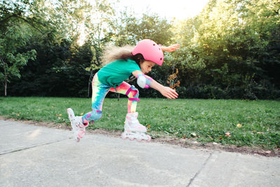 Happy caucasian girl in pink helmet riding in roller skates on road in park on summer day. 