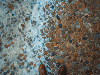 Low section of man standing on cobblestone during winter