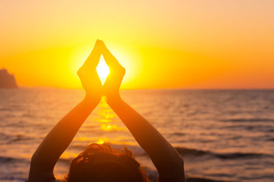 Cropped hand holding heart shape against orange sky