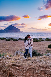 Friends standing on beach against sky during sunset