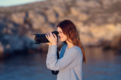 Side view of woman photographing against blurred background