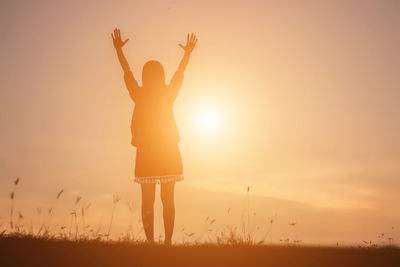 Low angle view of woman standing on field against sky during sunset