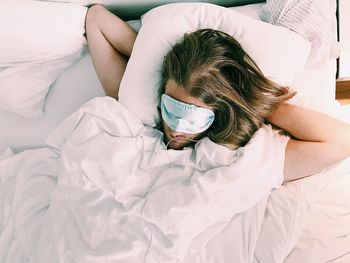 High angle view of man wearing sleep mask on bed at home