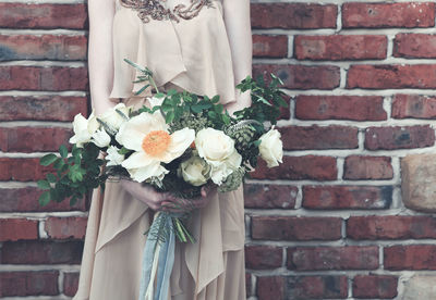 Midsection of woman holding bouquet against wall