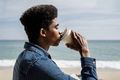 Man drinking coffee at beach during sunny day