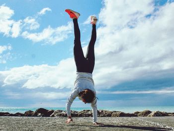 Man with arms raised on beach against sky