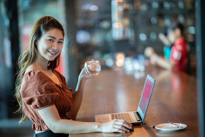 Portrait of smiling young woman using phone on table