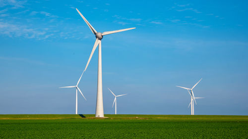 Windmills on field against blue sky