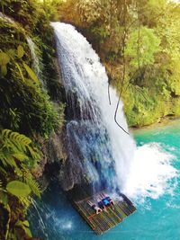 High angle view of people lying on wooden raft below waterfall