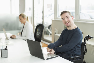 Portrait of happy businessman with cerebral palsy using laptop in office