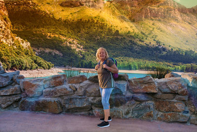 Full length portrait of woman standing against stone wall