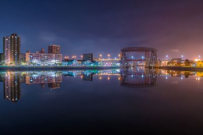 Illuminated buildings and puente transbordador reflection in matanza river against sky at night