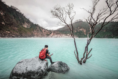 Person on rock by lake against sky