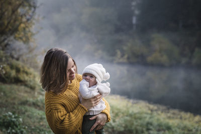 A woman is holding a baby near a river