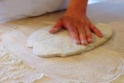 Cropped image of hand on pizza dough with flour at table