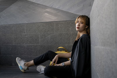 Portrait of young woman sitting against wall