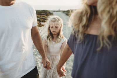 Serious girl making sad face walking with parents at beach