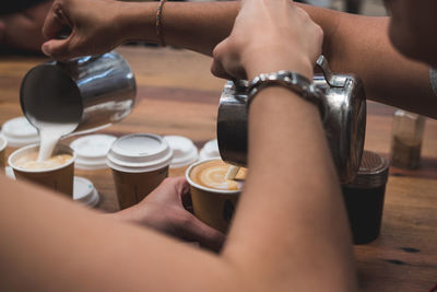 Cropped image of hands pouring milk in coffee