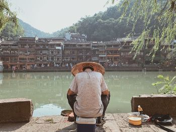 Rear view of woman standing by lake against trees