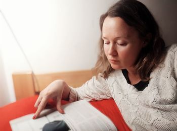 Young woman looking away while sitting on book at home