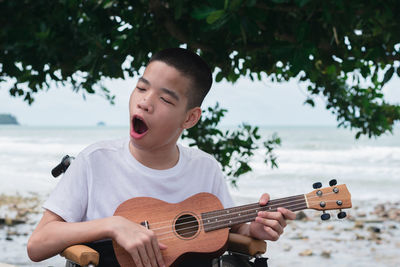 Cheerful boy playing ukulele against tree